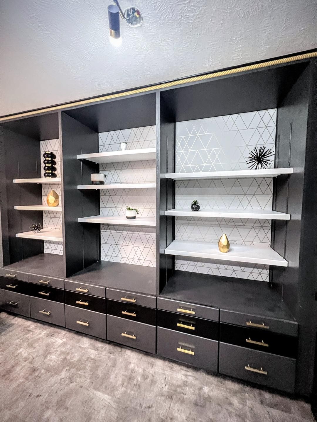 Built-in gray shelving unit with open shelves and drawers. Includes gold hardware, a decorative tile backsplash, and gold accents.
