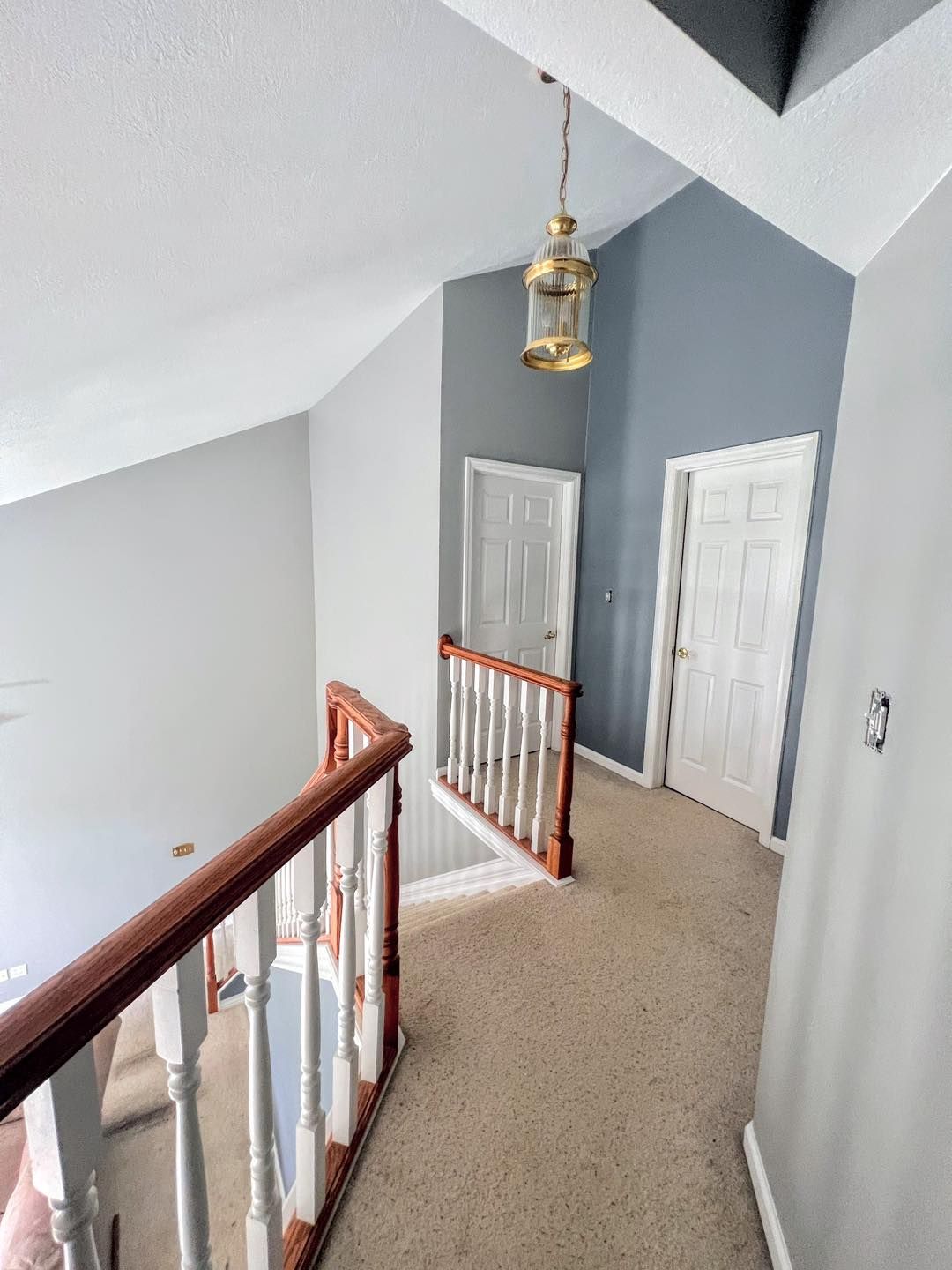 Interior hallway from a second floor. Carpeted floor, gray walls, and a wooden railing. Two white doors are visible.