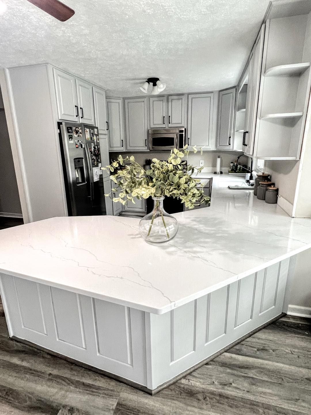 A modern kitchen with white cabinetry, a large island, and white quartz countertops. A vase of flowers sits on the island.