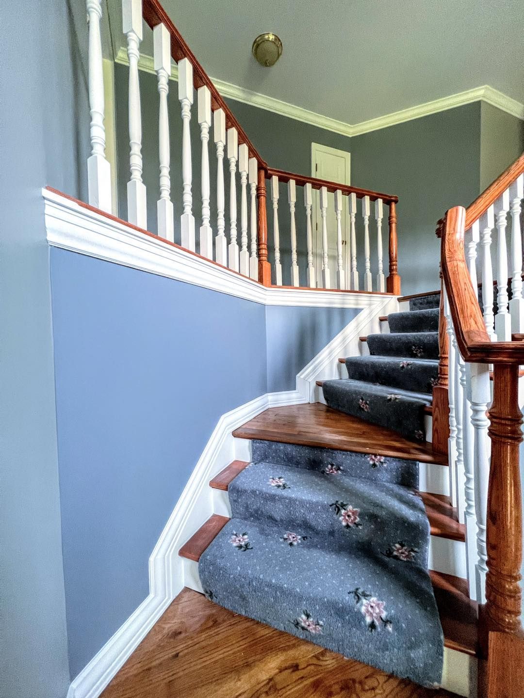 Staircase with wooden railings and blue carpet, leading to an upper level with grey walls and white trim.