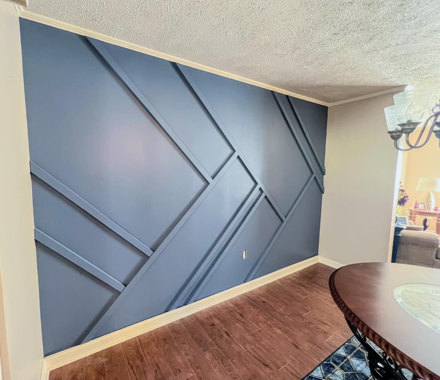 A navy blue accent wall with geometric wood trim in a dining area, with a brown table and wood floor.