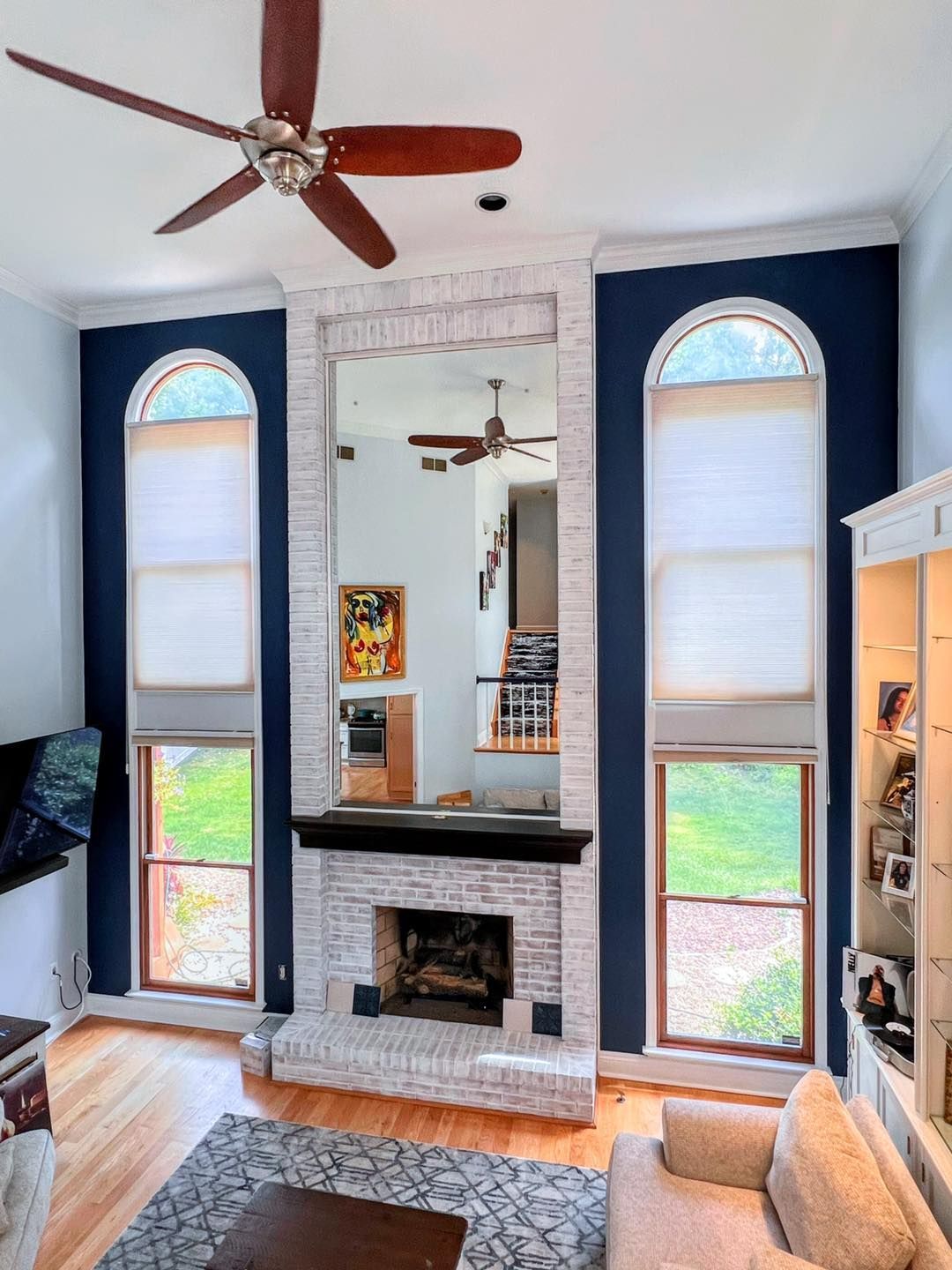 Living room with a fireplace, large mirror, and two arched windows with dark blue walls and white trim.
