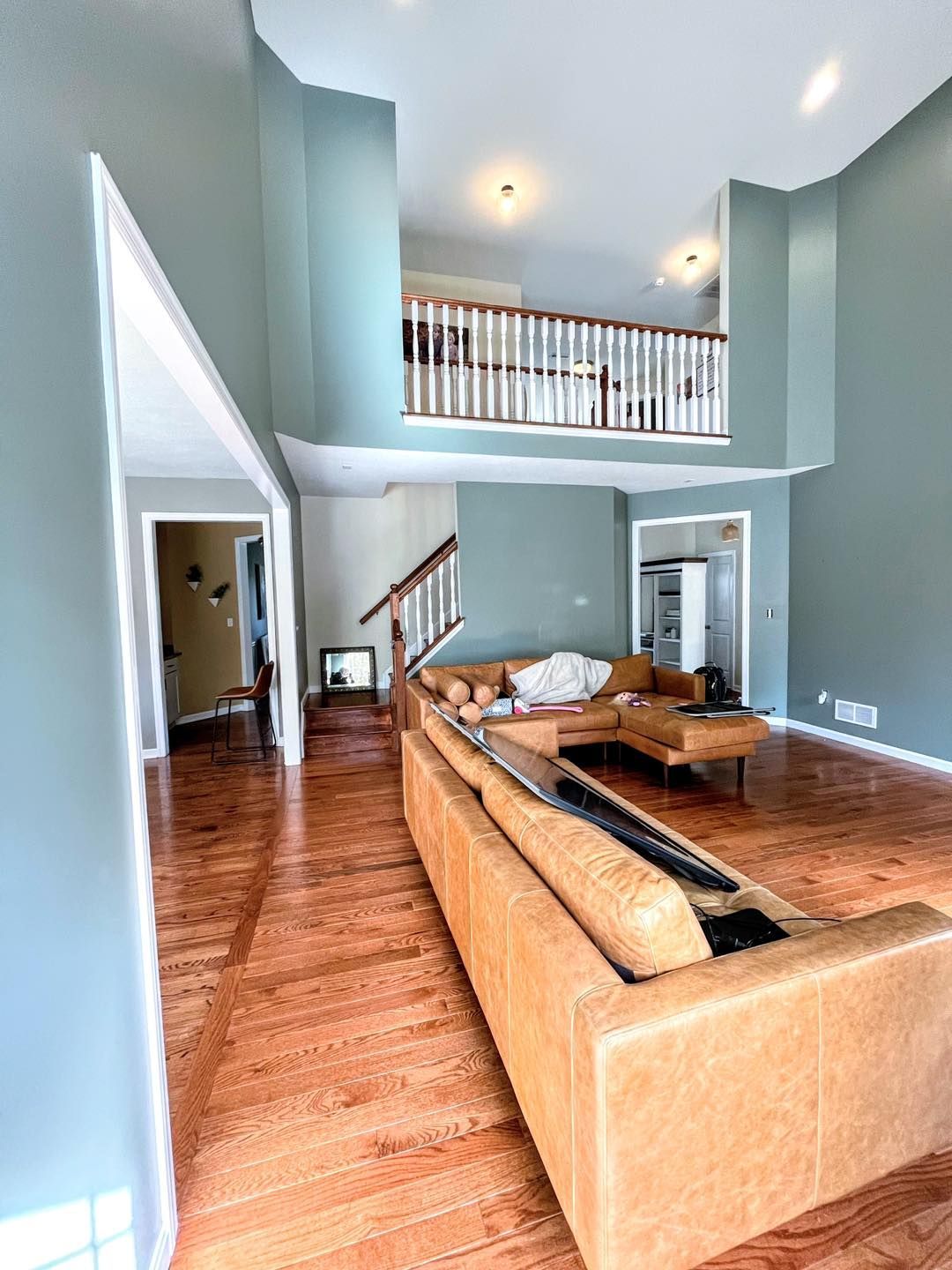 Spacious living room with light blue walls, wood floors, a large tan sectional sofa, and a loft area.
