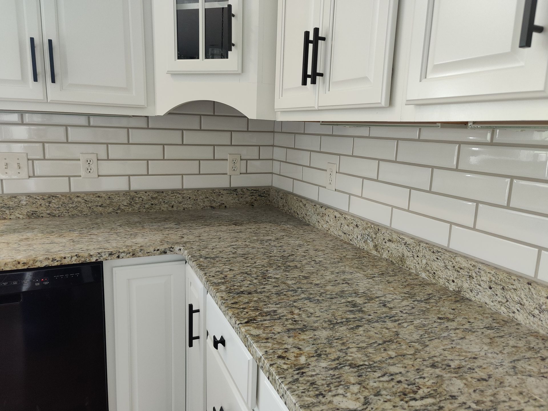 A kitchen corner with white cabinets, a granite countertop, and white subway tile backsplash. The cabinet hardware is black.