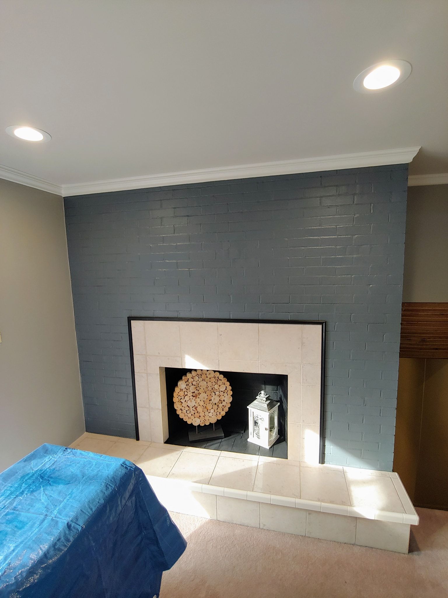 Fireplace with a dark blue painted brick wall and a white stone surround, with a decorative wooden circle and lantern inside the hearth.
