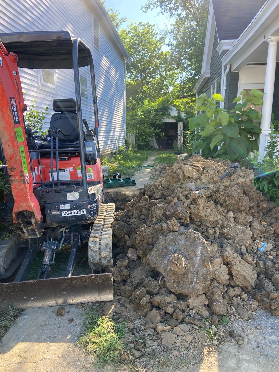 A small excavator is digging a hole in the dirt in front of a house.