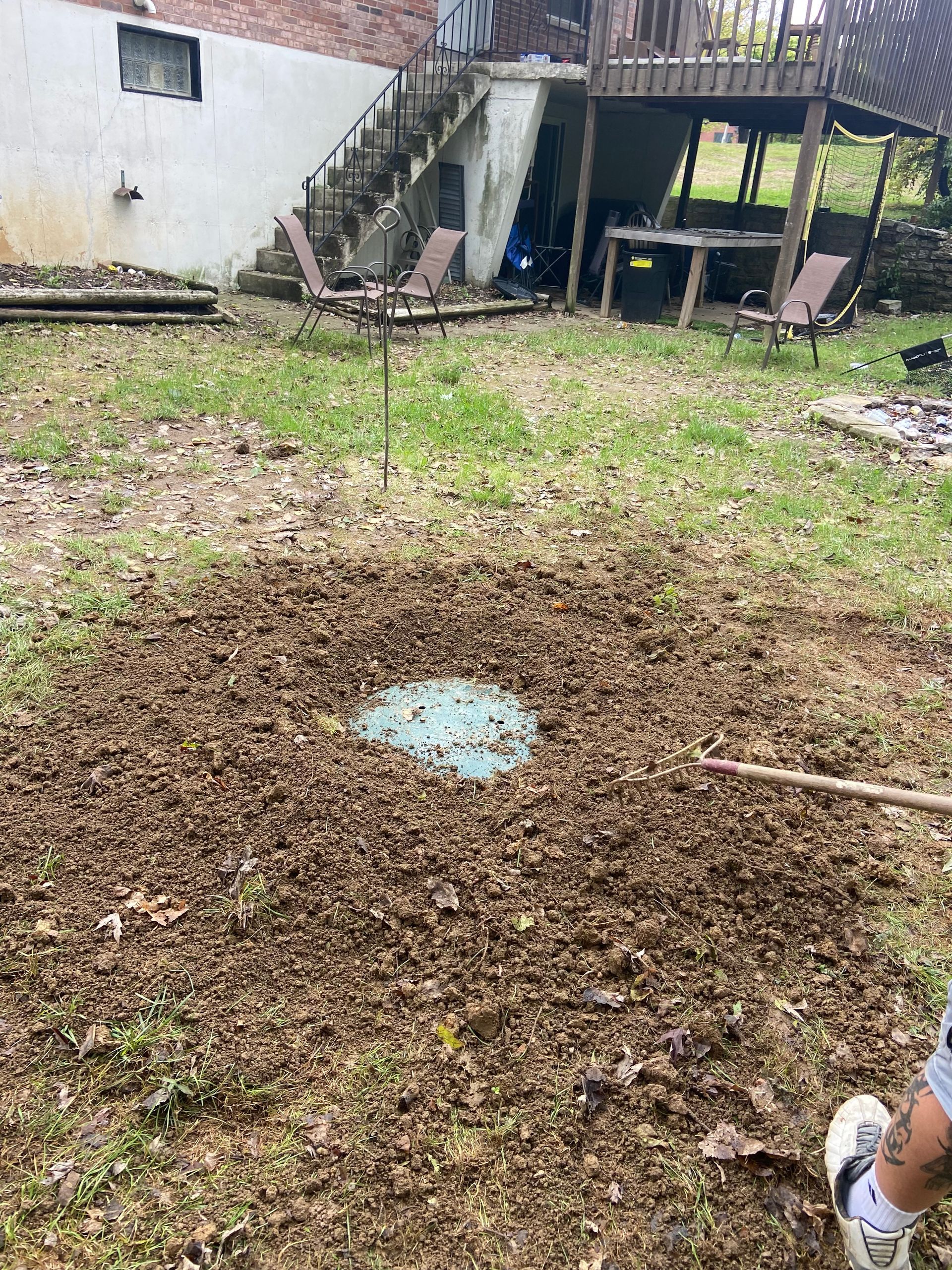A person is raking a pile of dirt in a backyard.