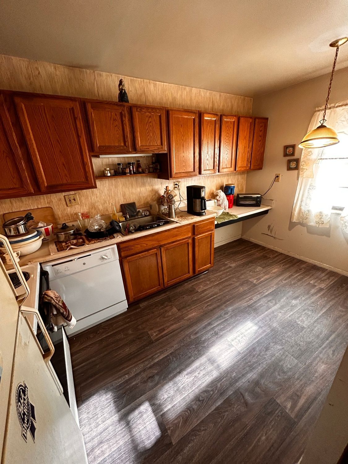 A kitchen with wooden cabinets , a white stove , a dishwasher , and a window.