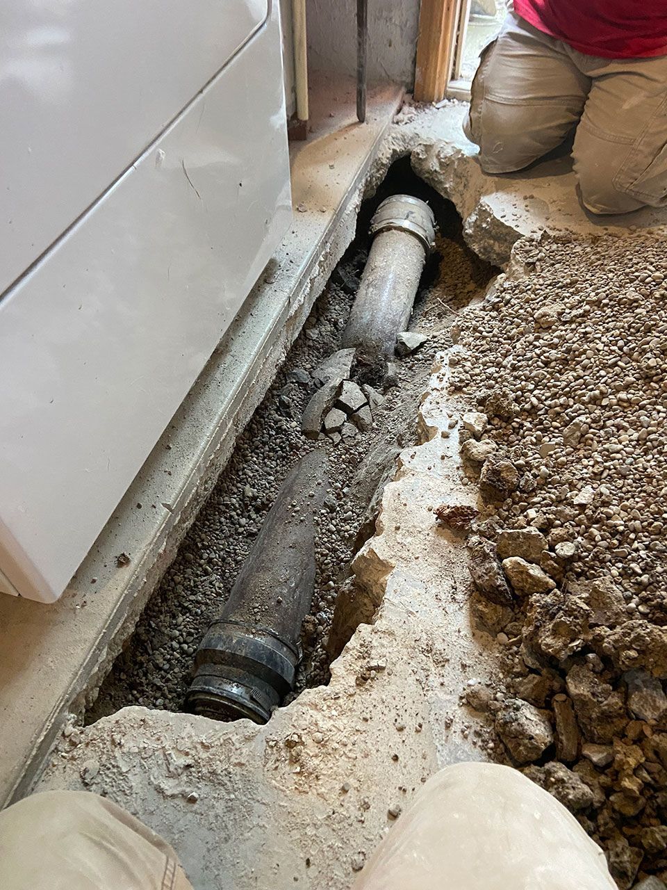 A person is kneeling down next to a pipe in the ground