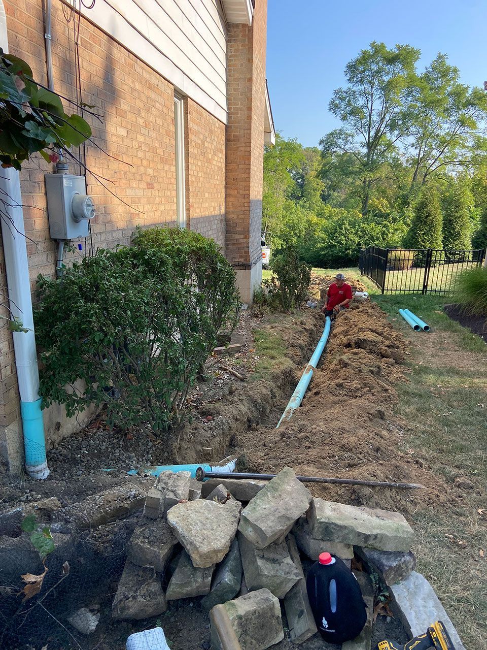 A man is laying pipes in the dirt in front of a house