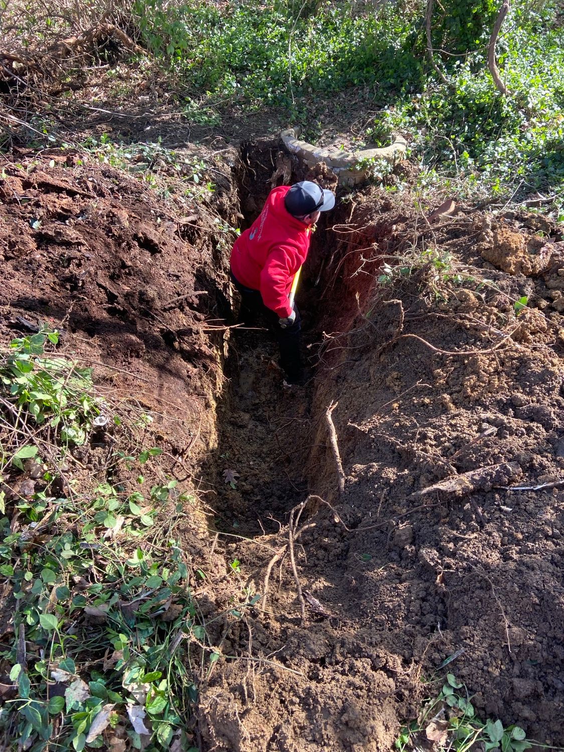 A man in a red jacket is digging a hole in the dirt.