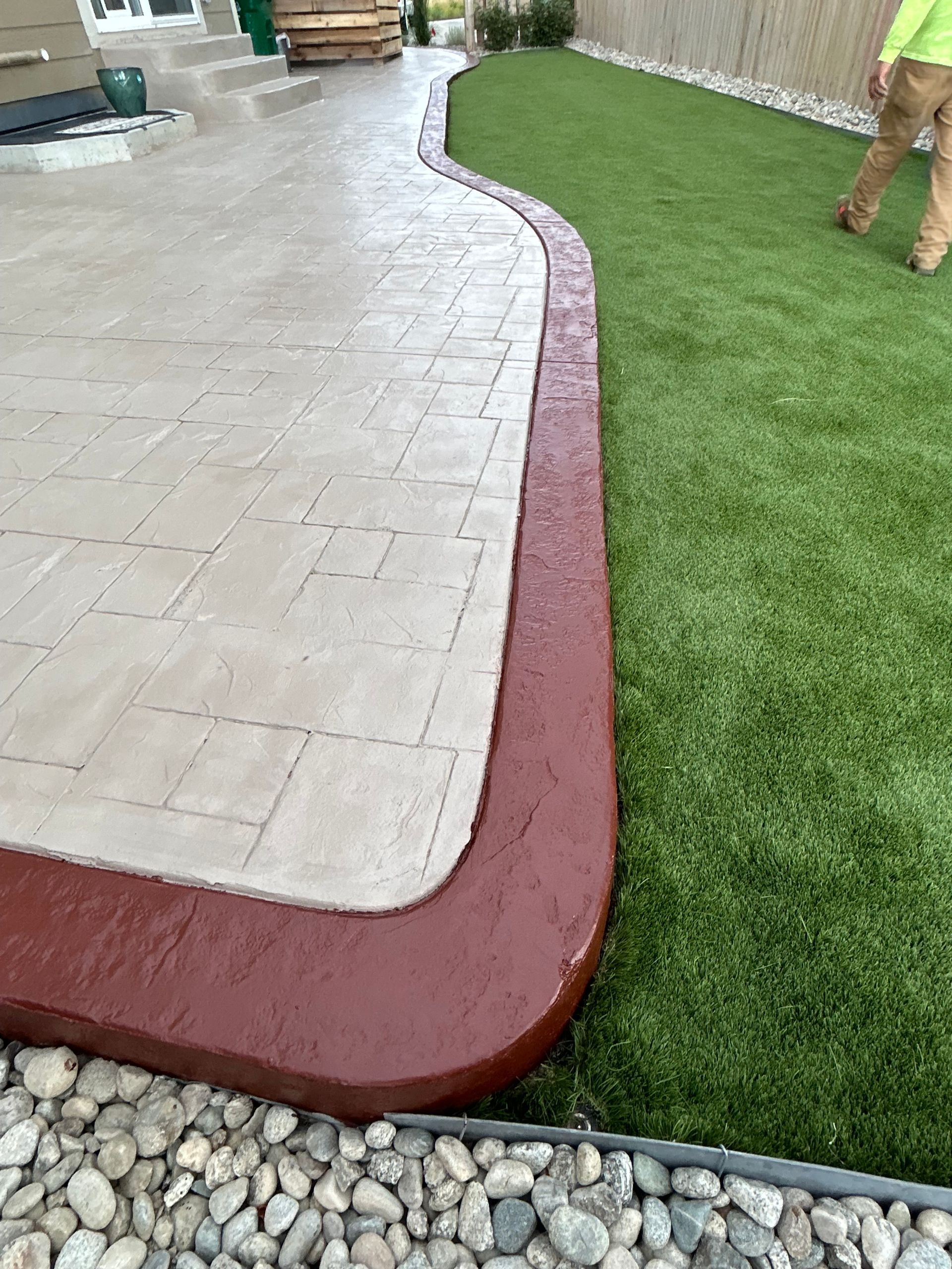 A man is standing next to a concrete patio with a red border.
