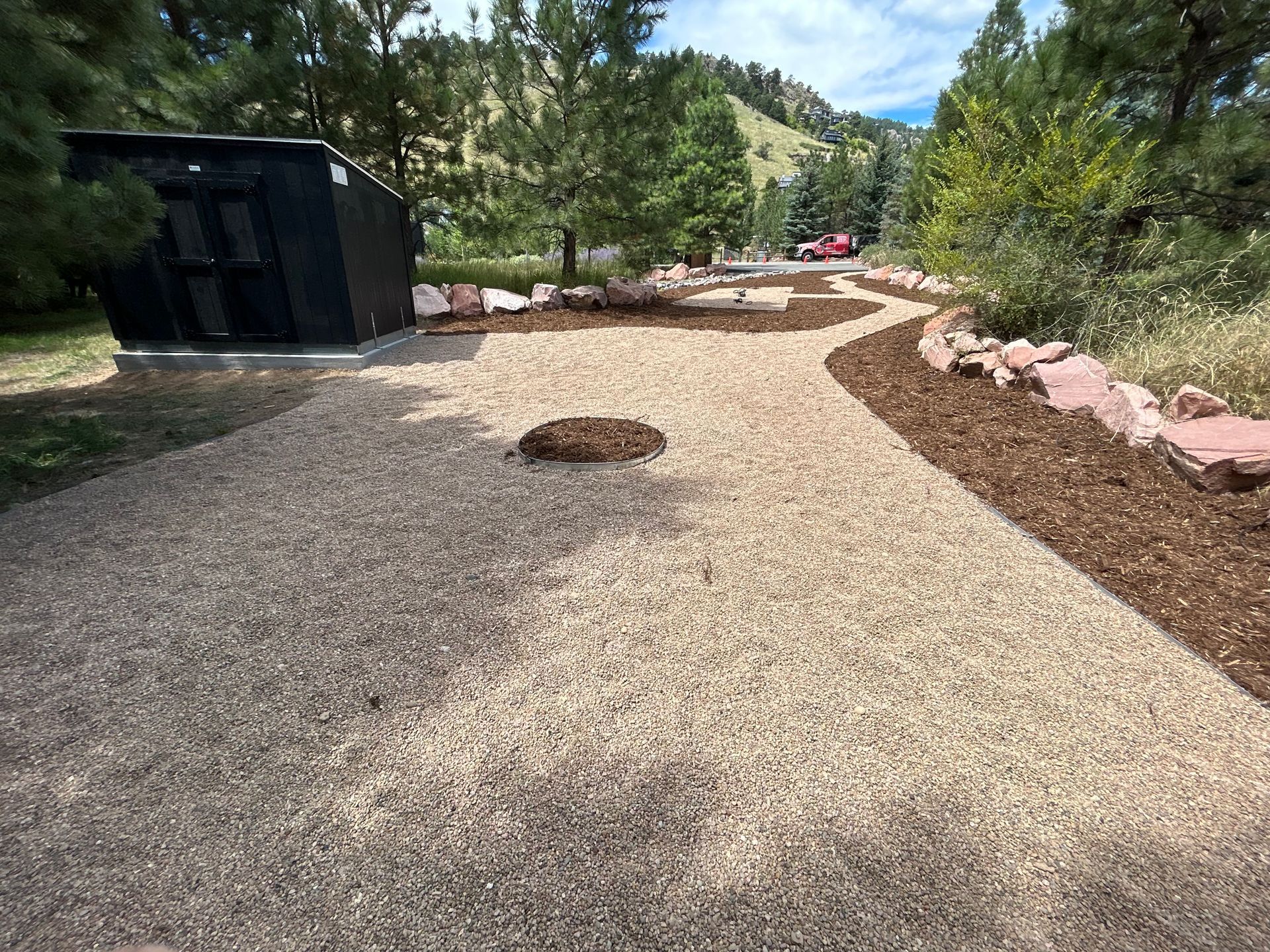 A gravel driveway leading to a shed in the woods.
