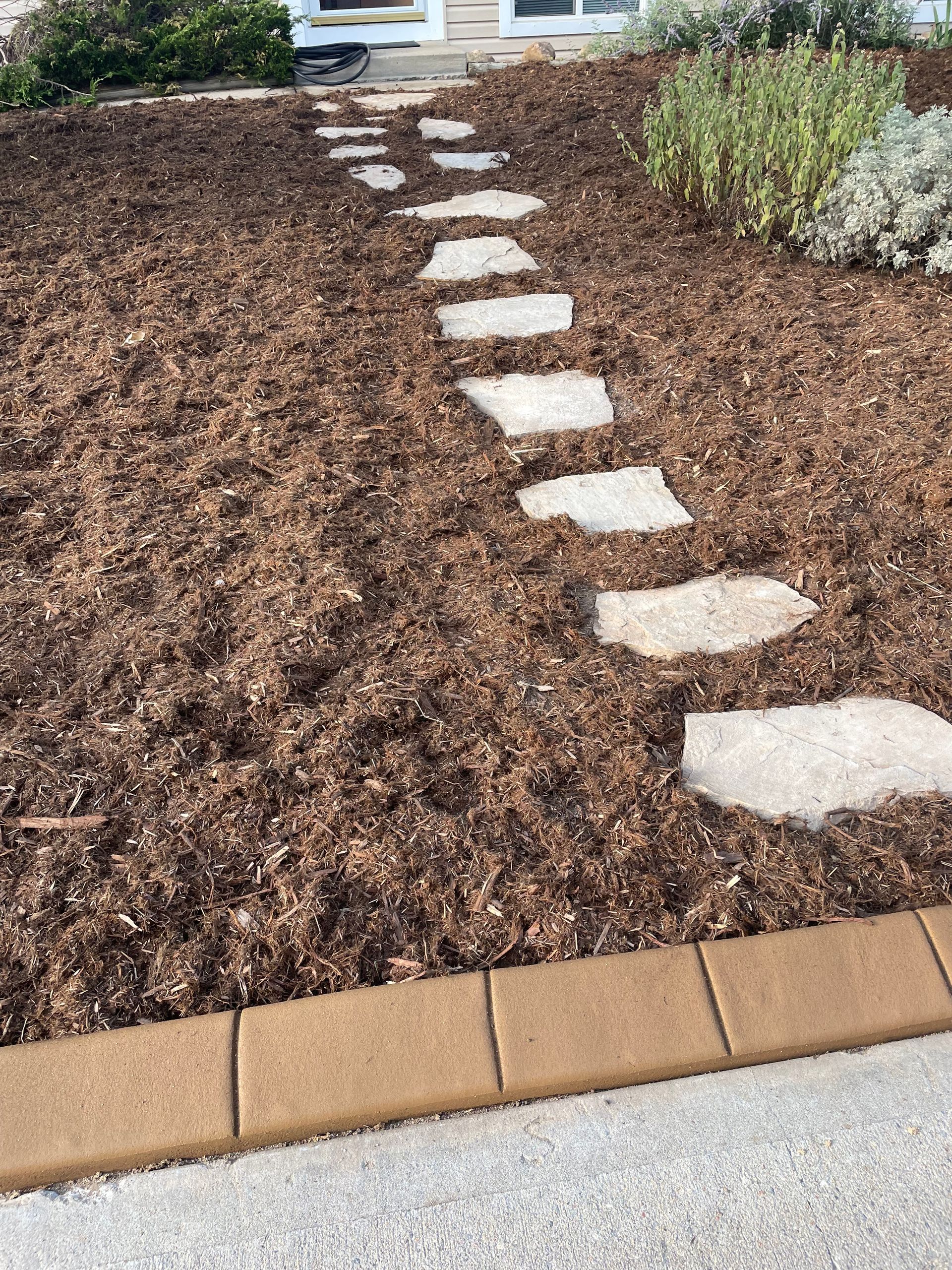 A stone walkway leading to a house in a garden.