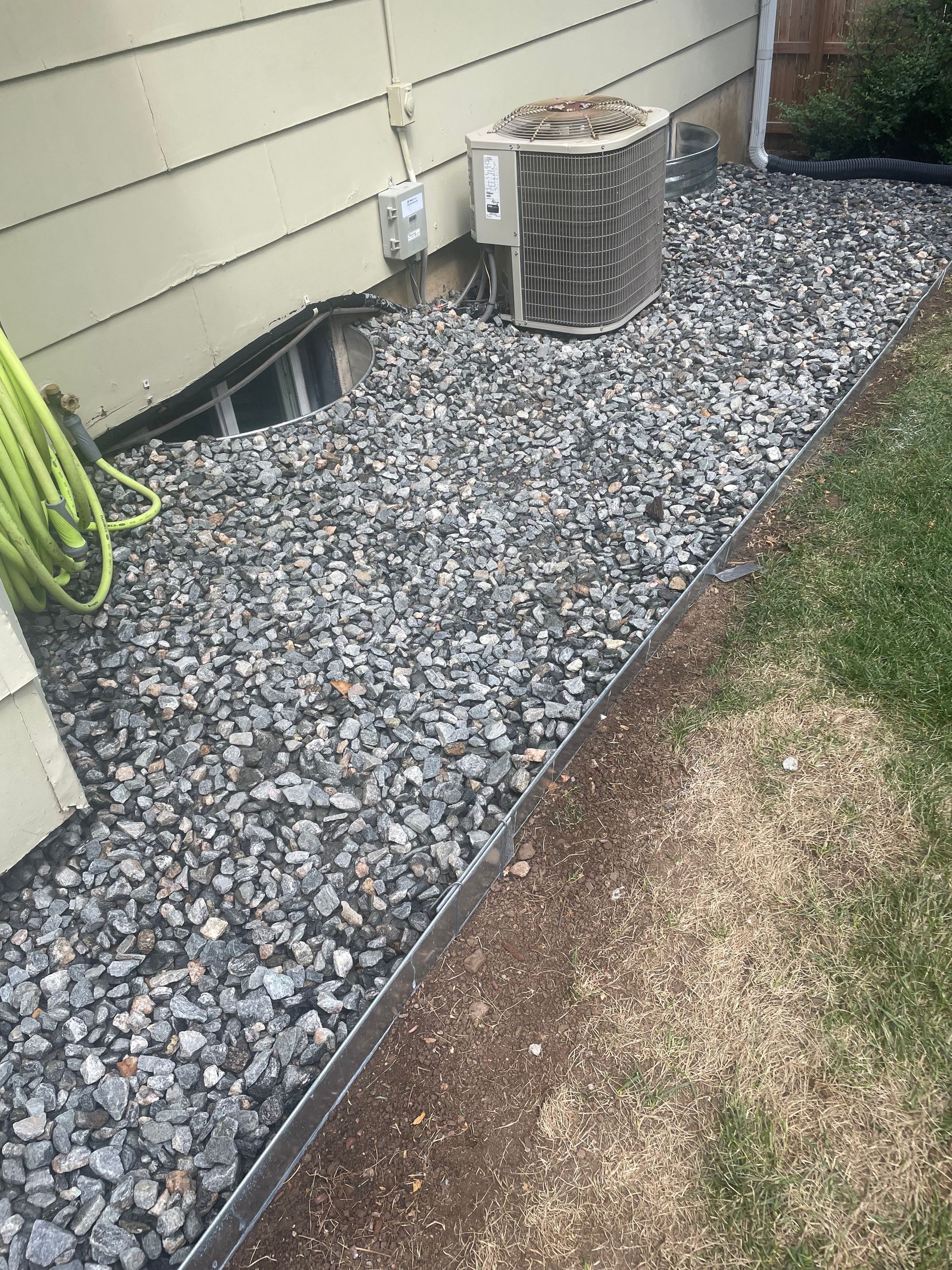 A hose is laying on a pile of gravel next to a house.