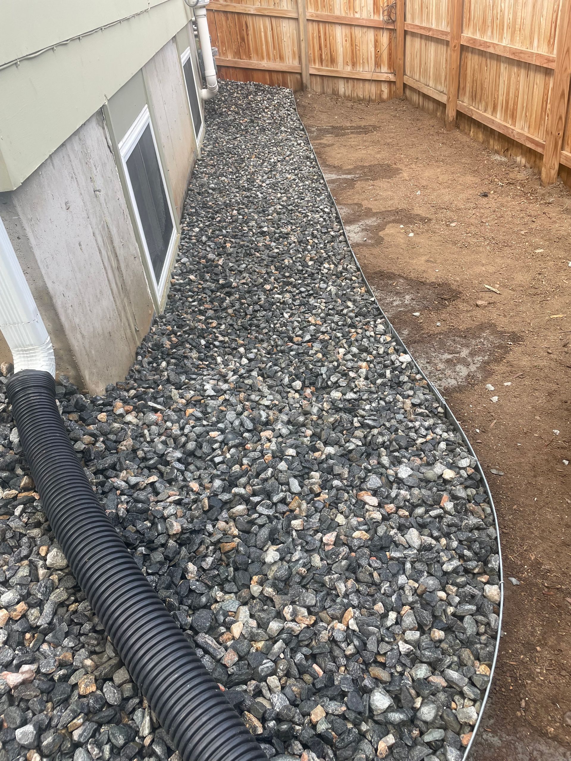 A black pipe is sitting on top of a pile of gravel next to a house.