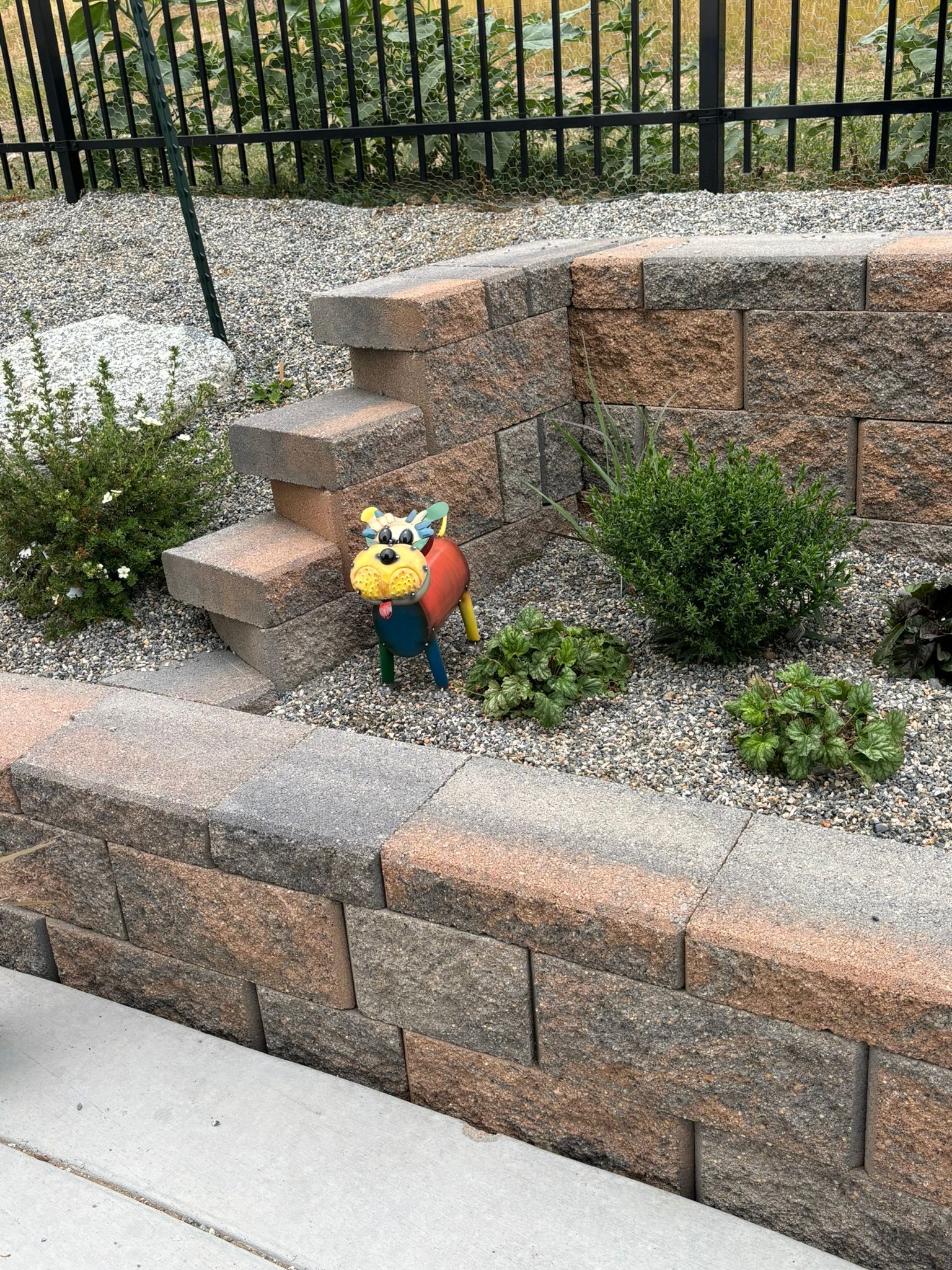 A dog statue is sitting in a garden next to a brick wall.