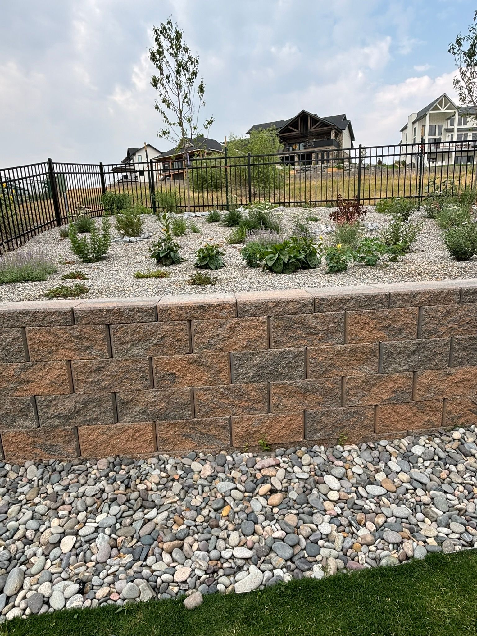 A brick wall surrounded by rocks and grass with a fence in the background.