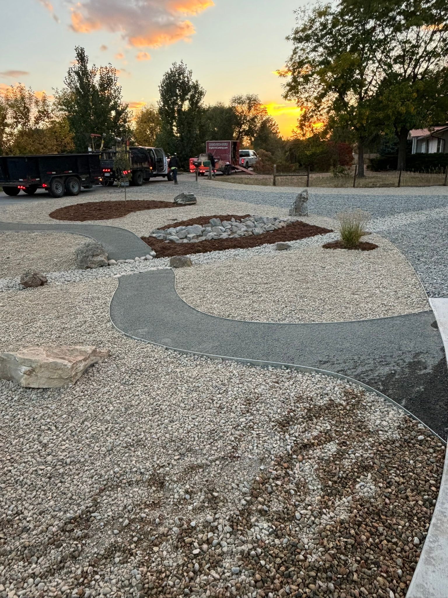 A gravel driveway with a truck parked in the background and a sunset in the background.
