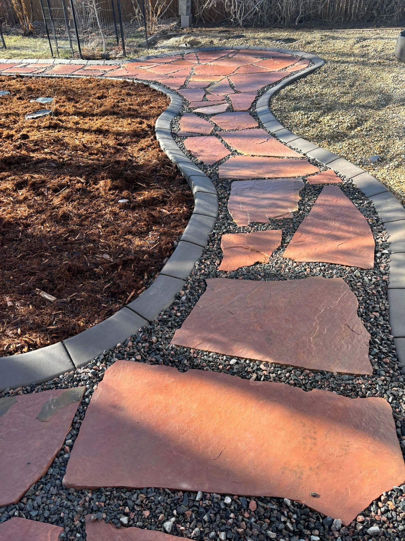 A stone walkway in a backyard surrounded by rocks and mulch.
