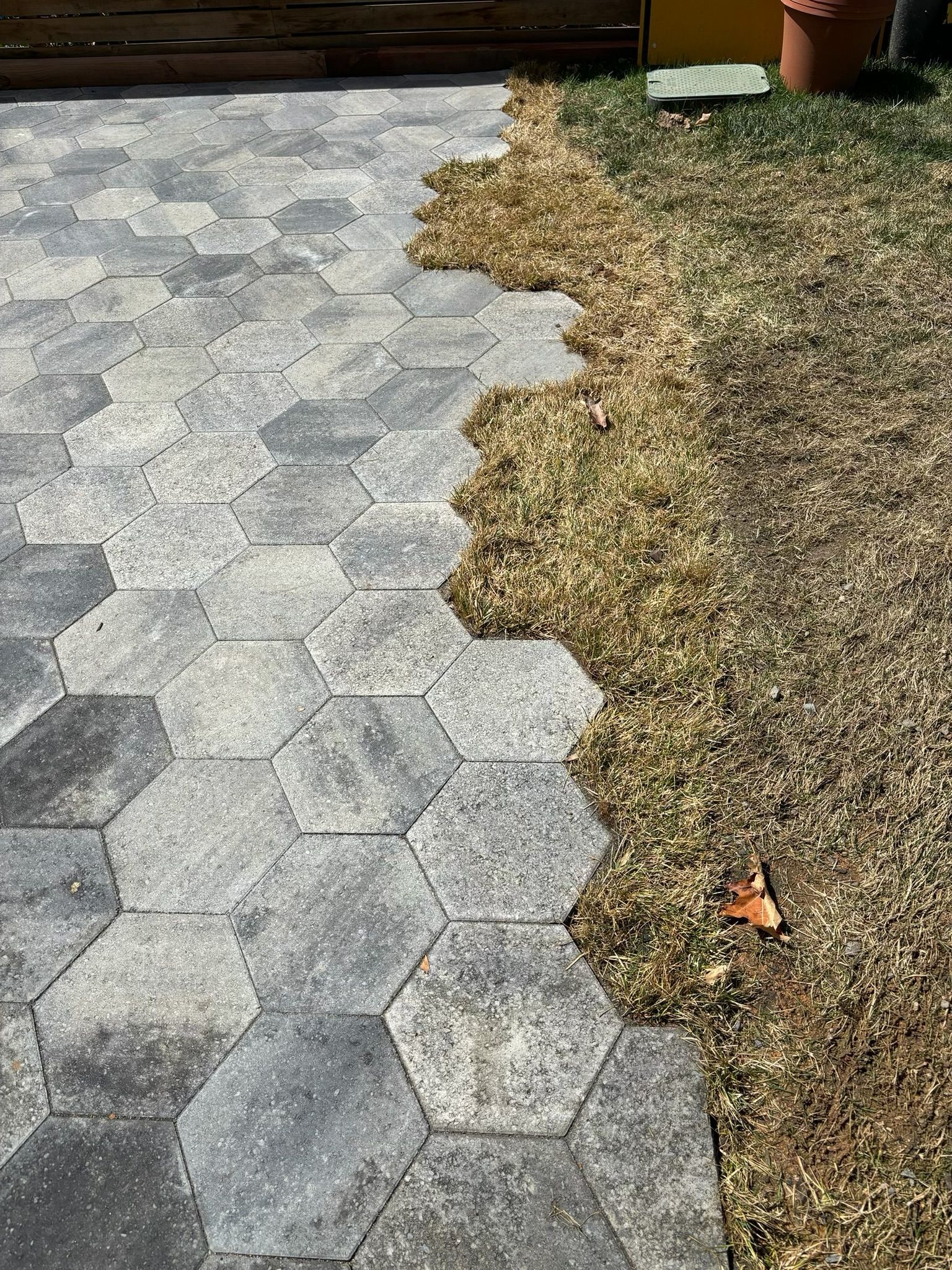 A patio with a hexagon pattern is being built next to a lawn.