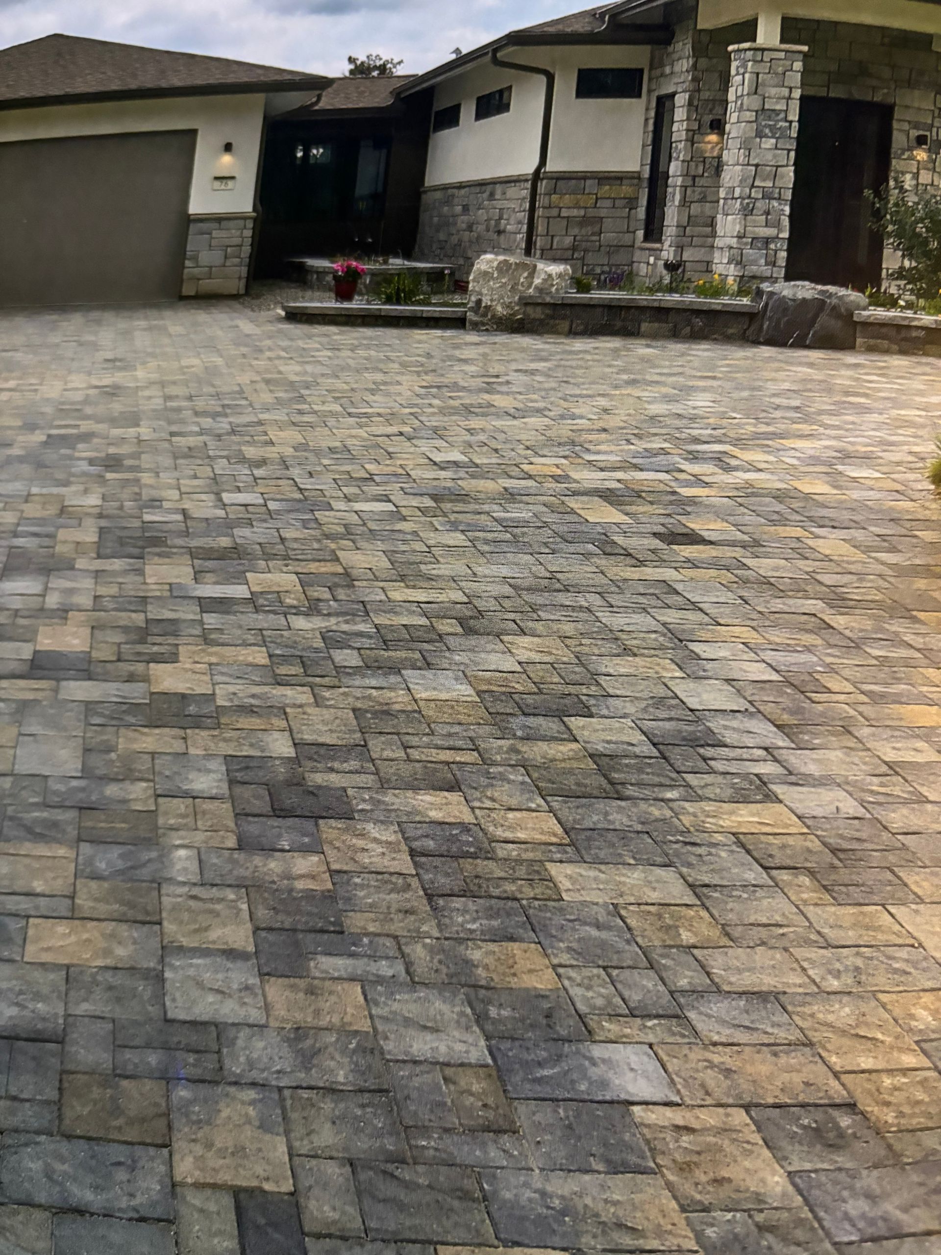 A stone-paved driveway leads to the entrance of a modern home with stone accents and an attached garage.