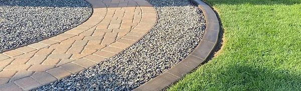 A brick walkway surrounded by gravel and grass in a backyard.