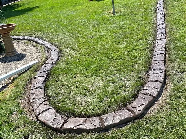 A concrete curb is sitting in the middle of a lush green lawn.
