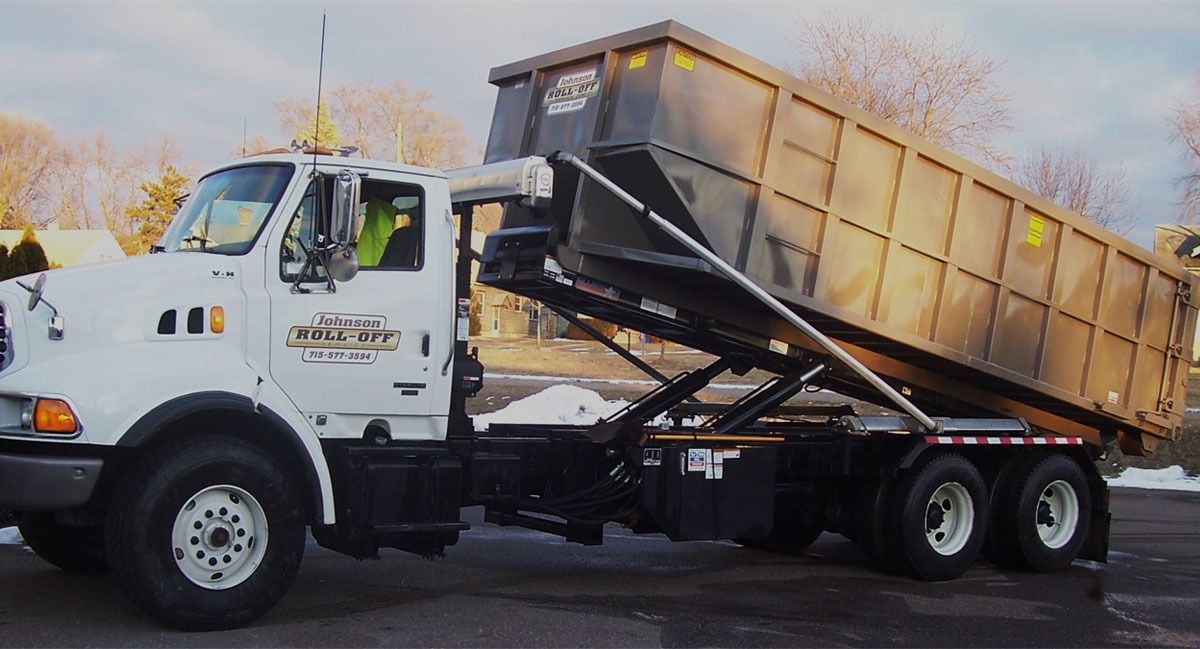 White dump truck with black container is raised to dump contents, snowy background.
