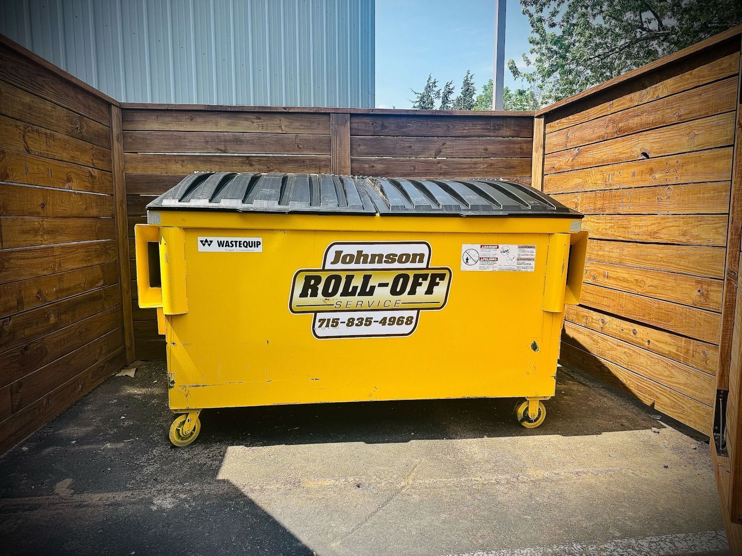 Yellow Johnson Roll-Off dumpster in a wooden enclosure.