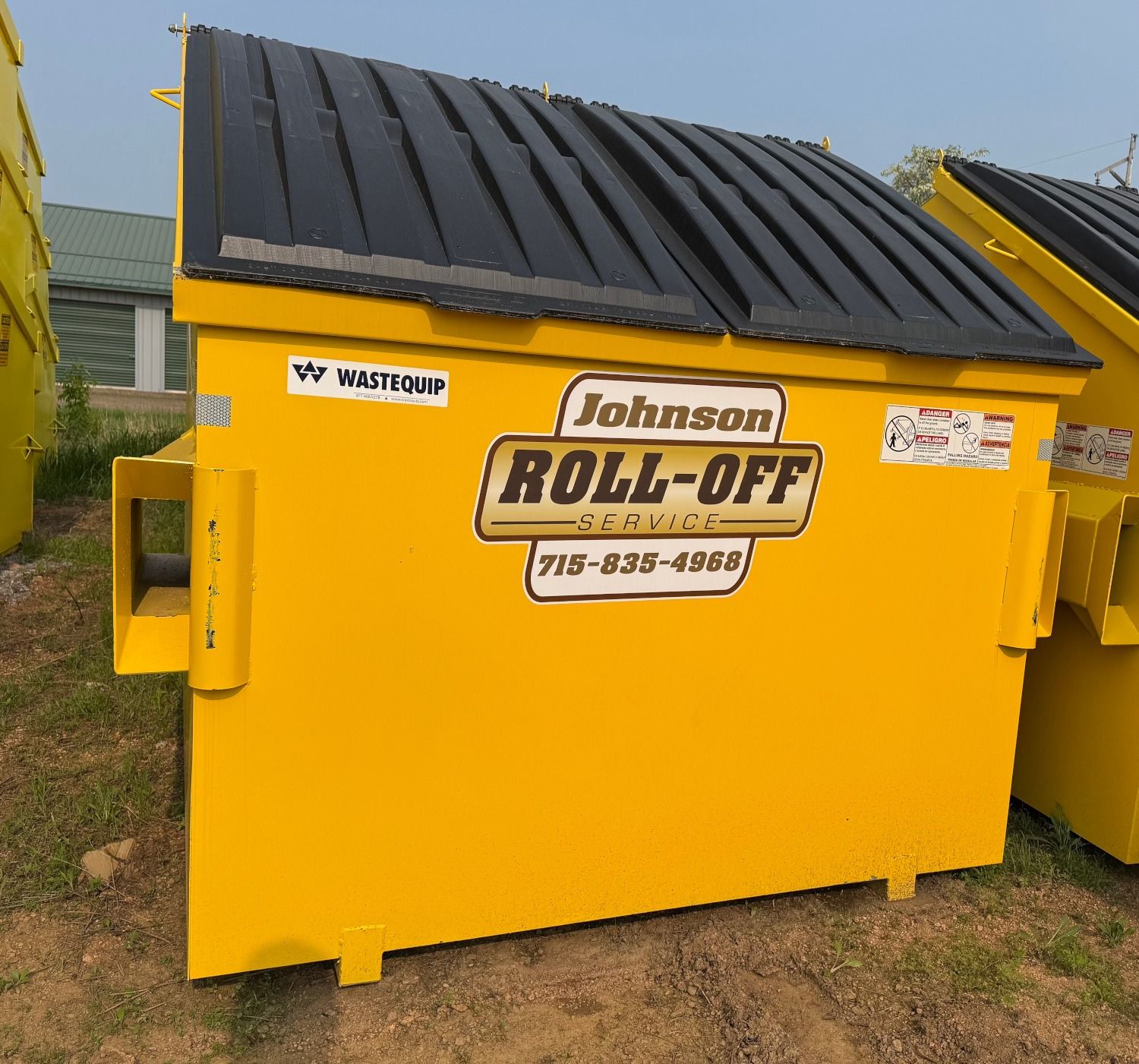 Yellow Johnson Roll-Off dumpster with black lid, outdoors.