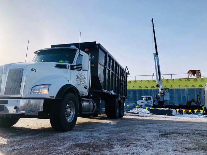 A white dump truck parked at a construction site beside a crane and a yellow barrier wall
