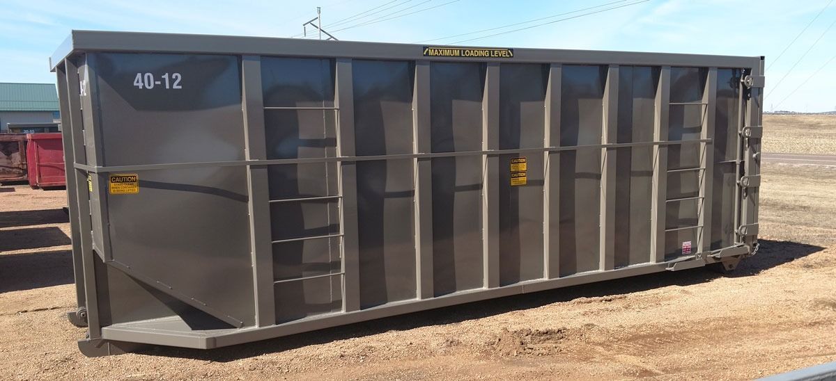 A large, rectangular gray metal dumpster on a dirt surface. 