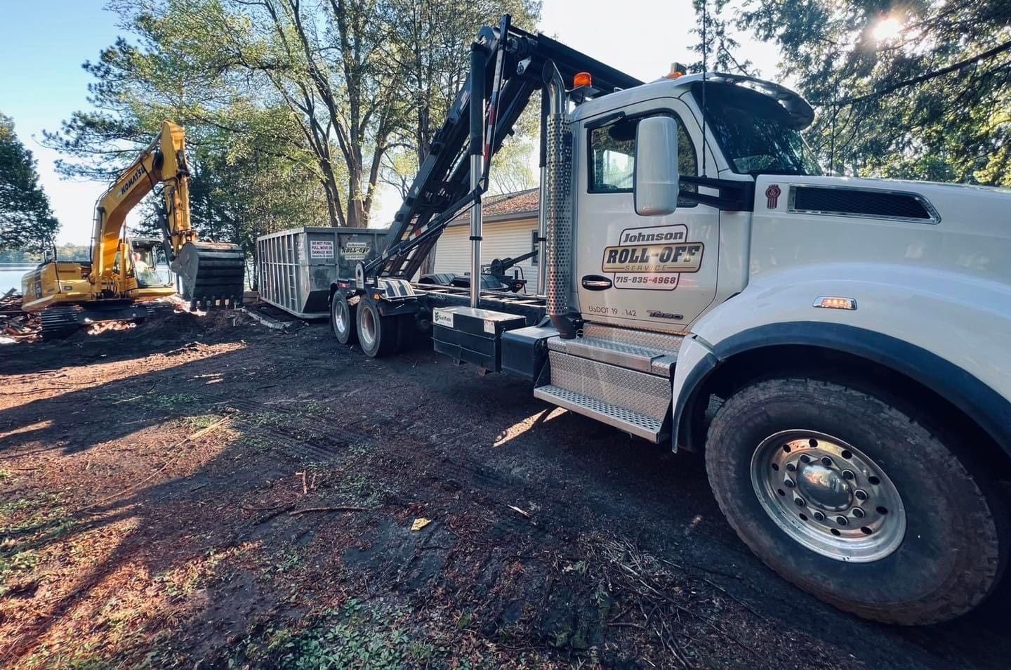 Truck with a raised arm lifting a dumpster with an excavator in the background. Construction site.