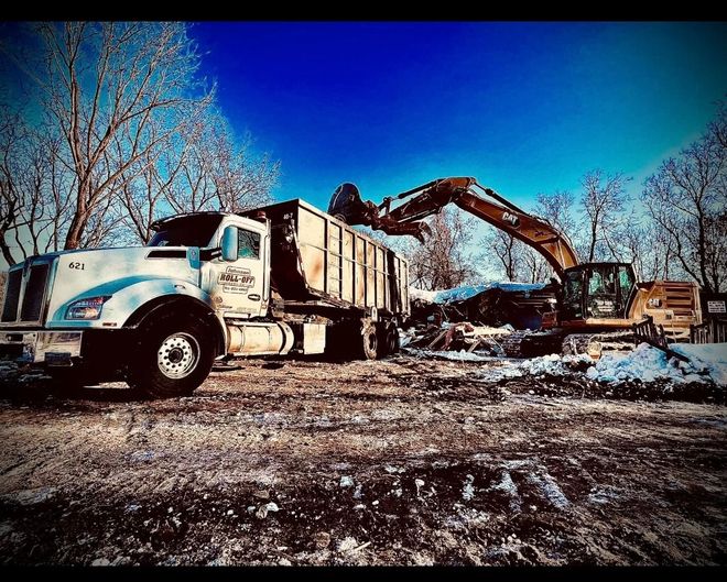 Blue dumpster being loaded with trash by a truck, outdoors.