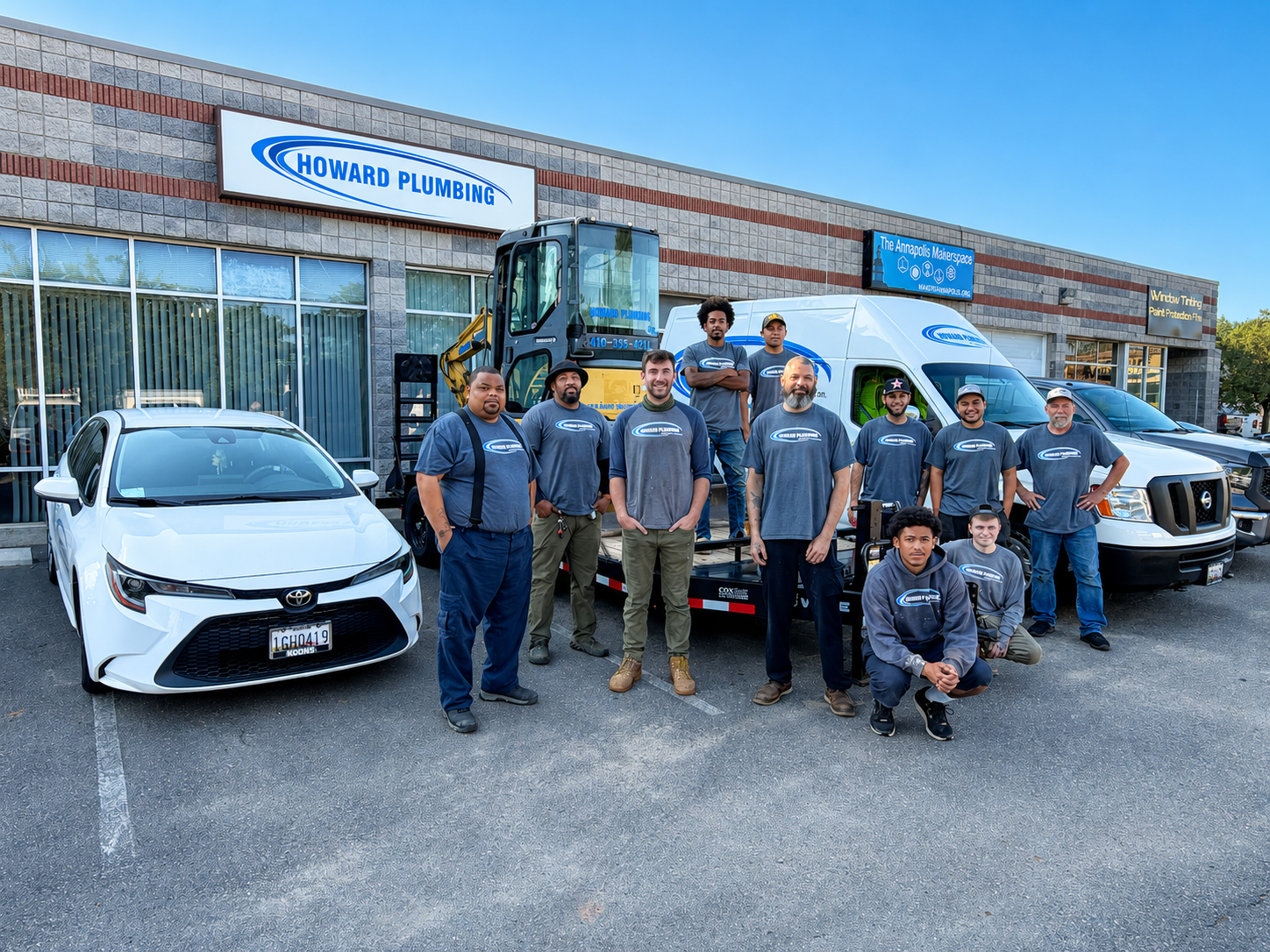 Group of workers posing outside a brick building with service vans and a white car in front