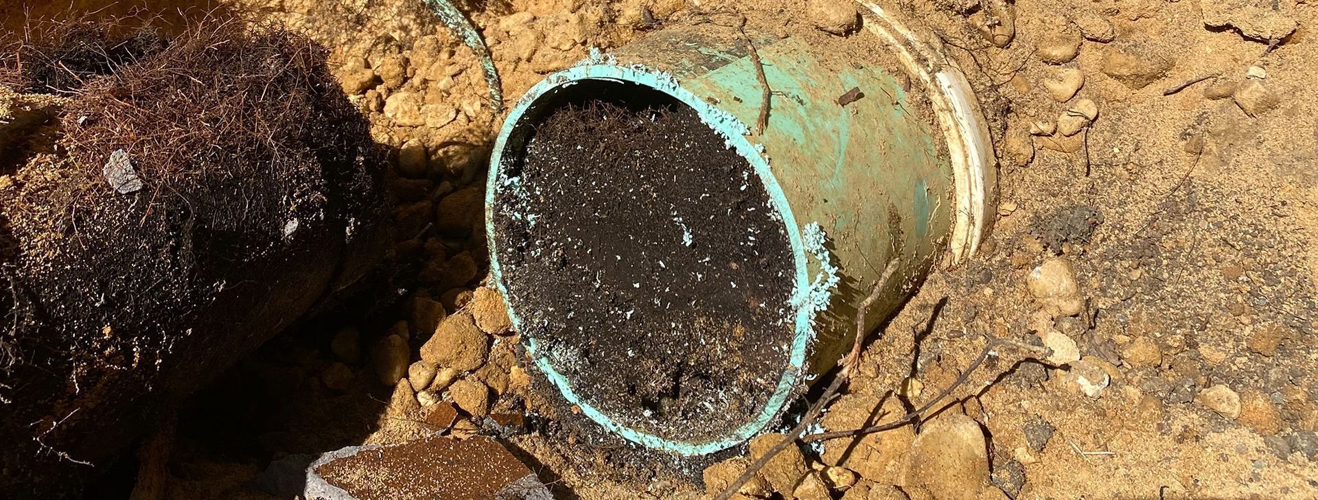 A section of light green, soil-filled PVC pipe sits partially buried in loose, brown dirt.
