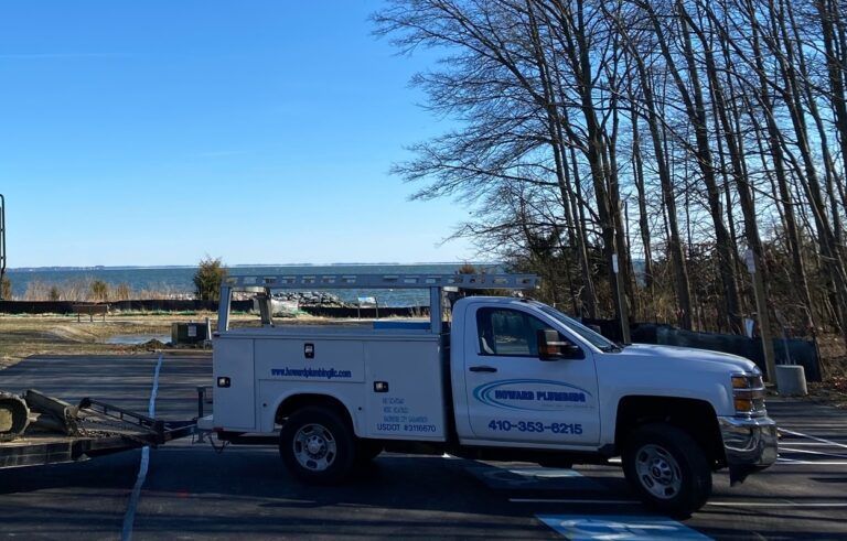 A white utility truck with a ladder rack and company branding parked on an asphalt lot near trees and water.