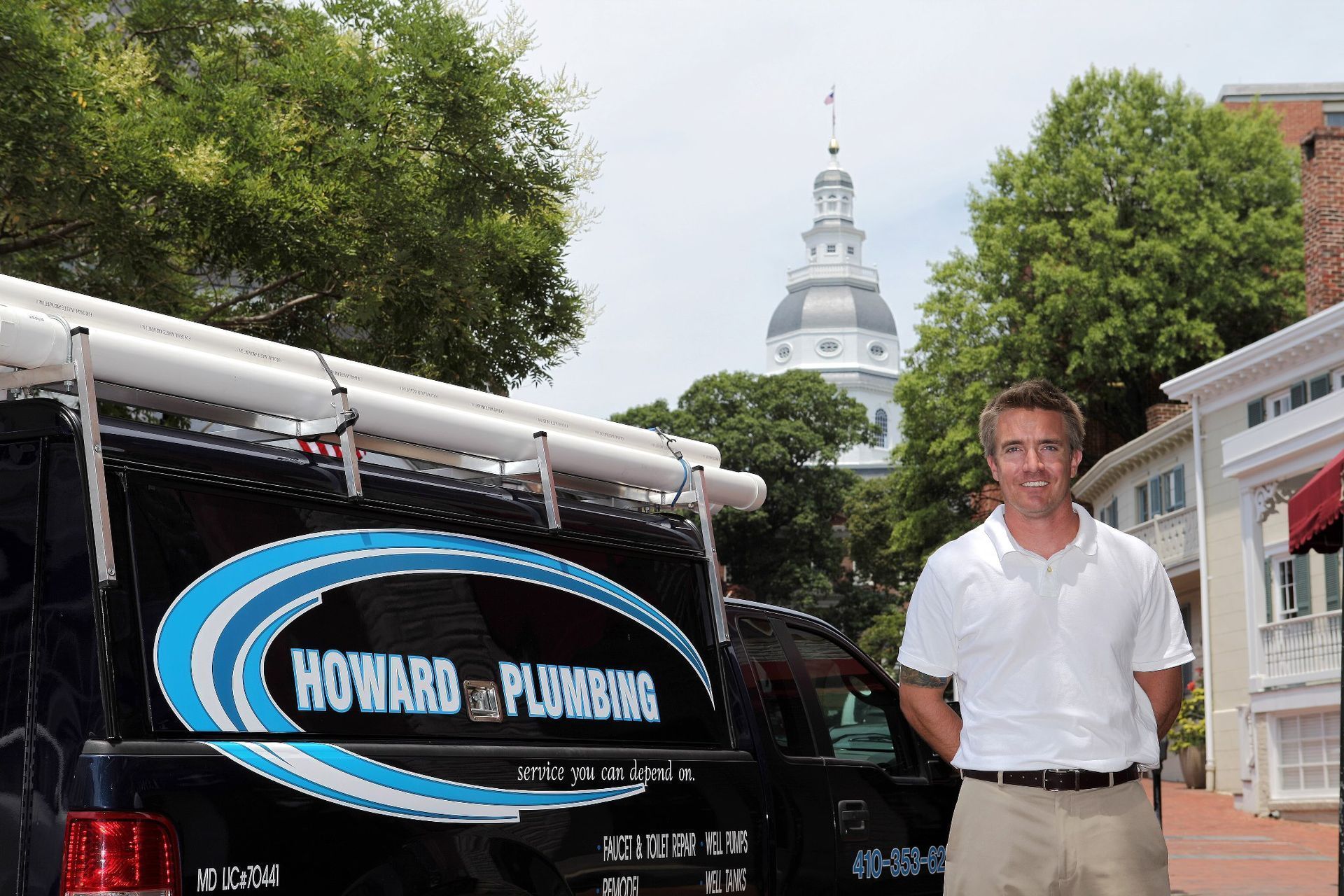 A person standing next to a black Howard Plumbing service van in front of the Maryland State House in Annapolis.