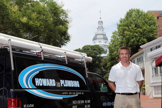 A person stands beside a Howard Plumbing service van in front of the Maryland State House dome.