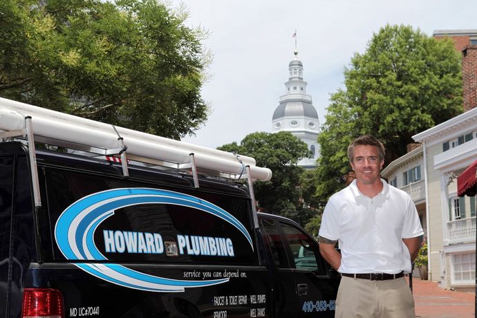 A person standing next to a black Howard Plumbing service van in front of the Maryland State House in Annapolis.