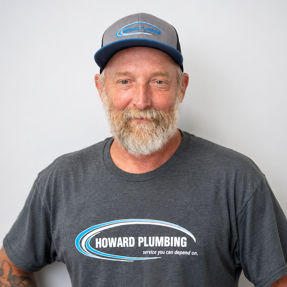 Man in a gray Howard Plumbing T-shirt and cap, smiling against a plain white background