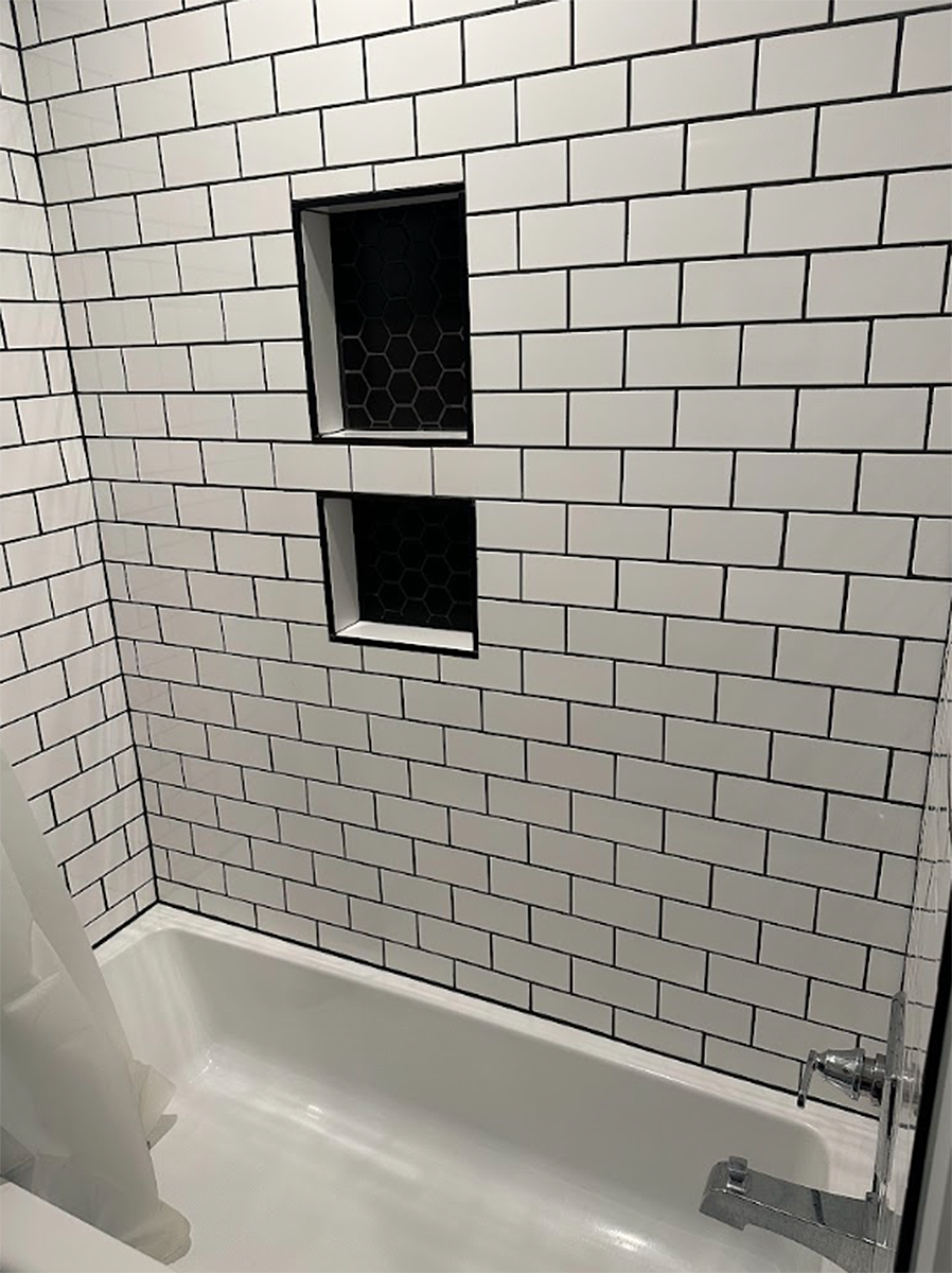 Bathroom tub with white subway-tile wall and two small black-framed recessed windows or niches