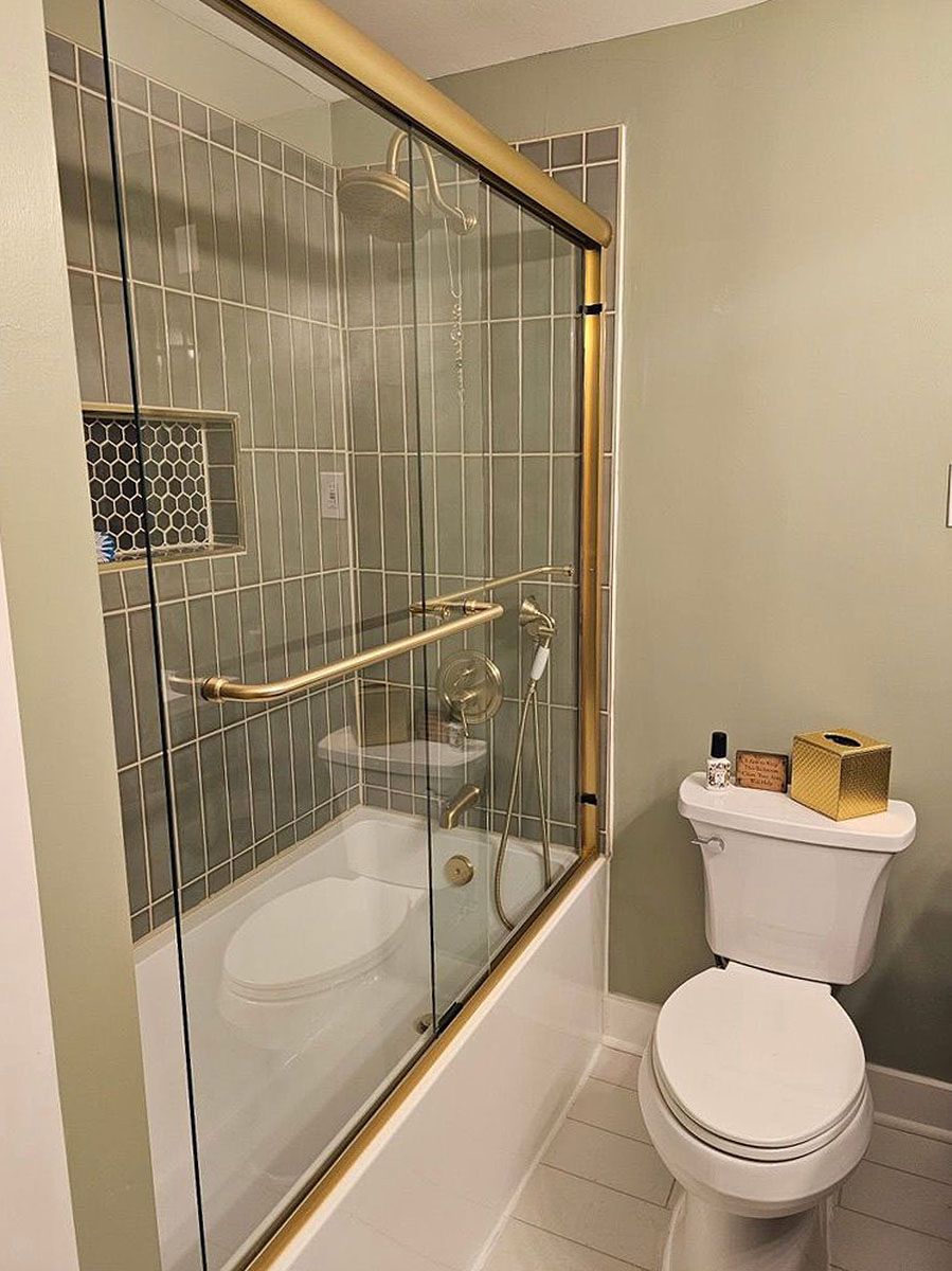 Small bathroom with a glass shower, beige walls, and a toilet topped with toiletries and a basket.