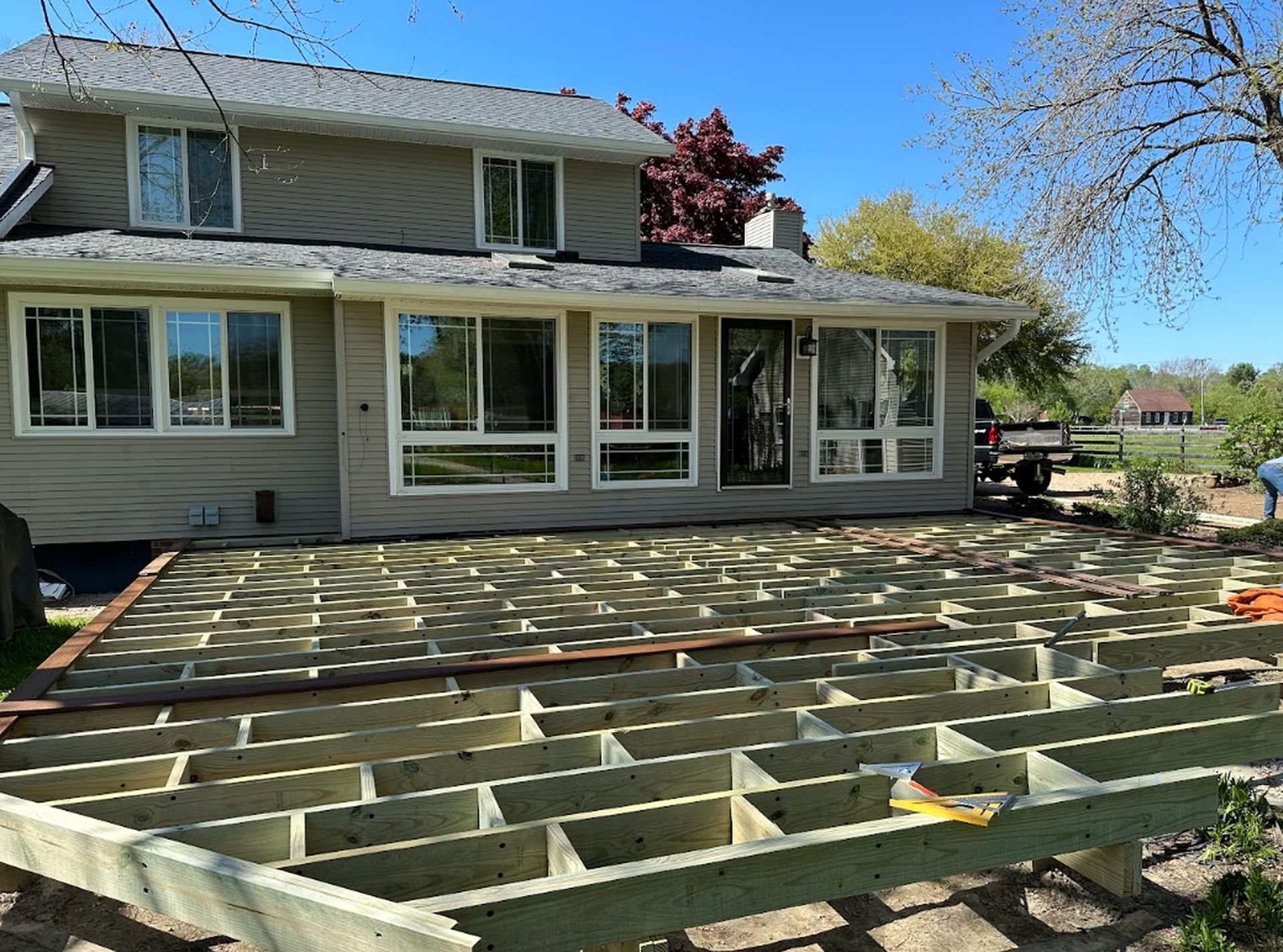 Backyard deck under construction beside a two-story house, with exposed wooden joists and a covered patio.