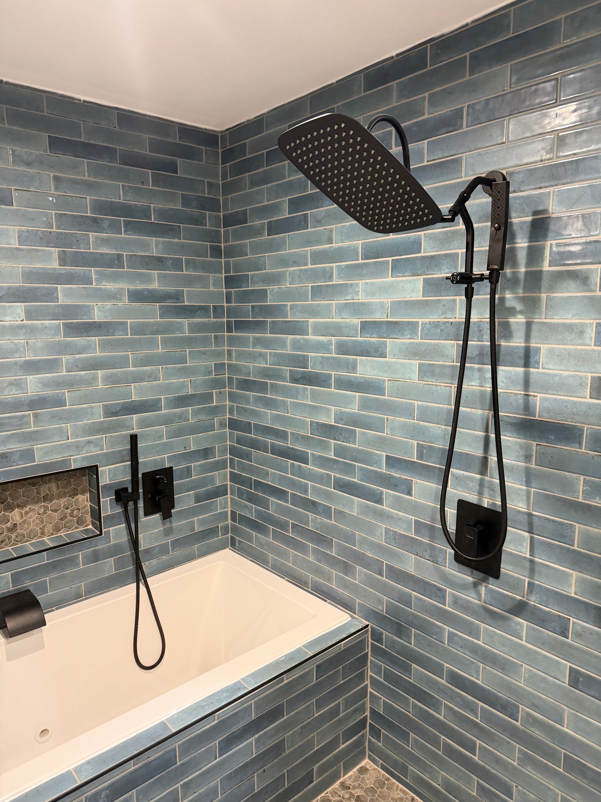 Corner shower with blue tile walls, white tub, and black showerhead and controls