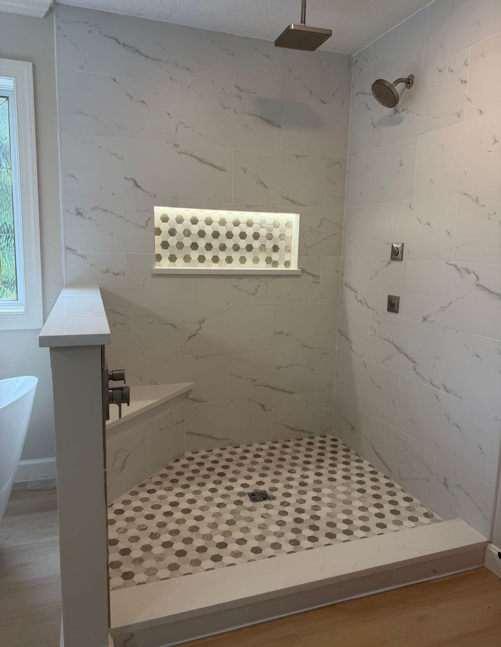 Walk-in shower with white marble-look tile, pebble floor, built-in niche, and glass window.