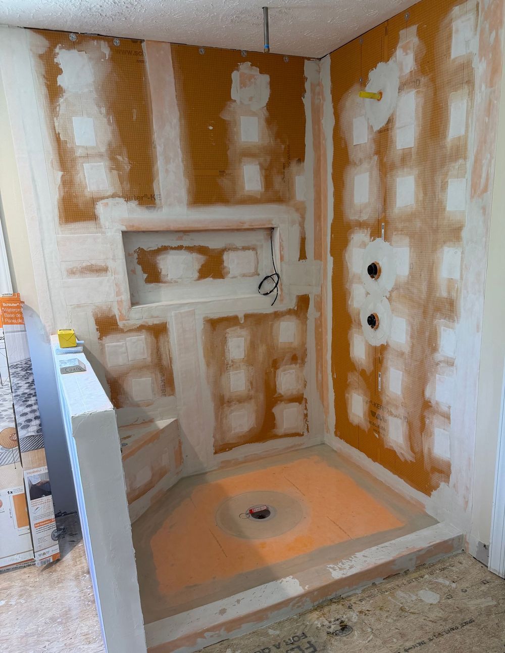 Partially renovated shower stall with orange-brown drywall patching and a new drain pan installed
