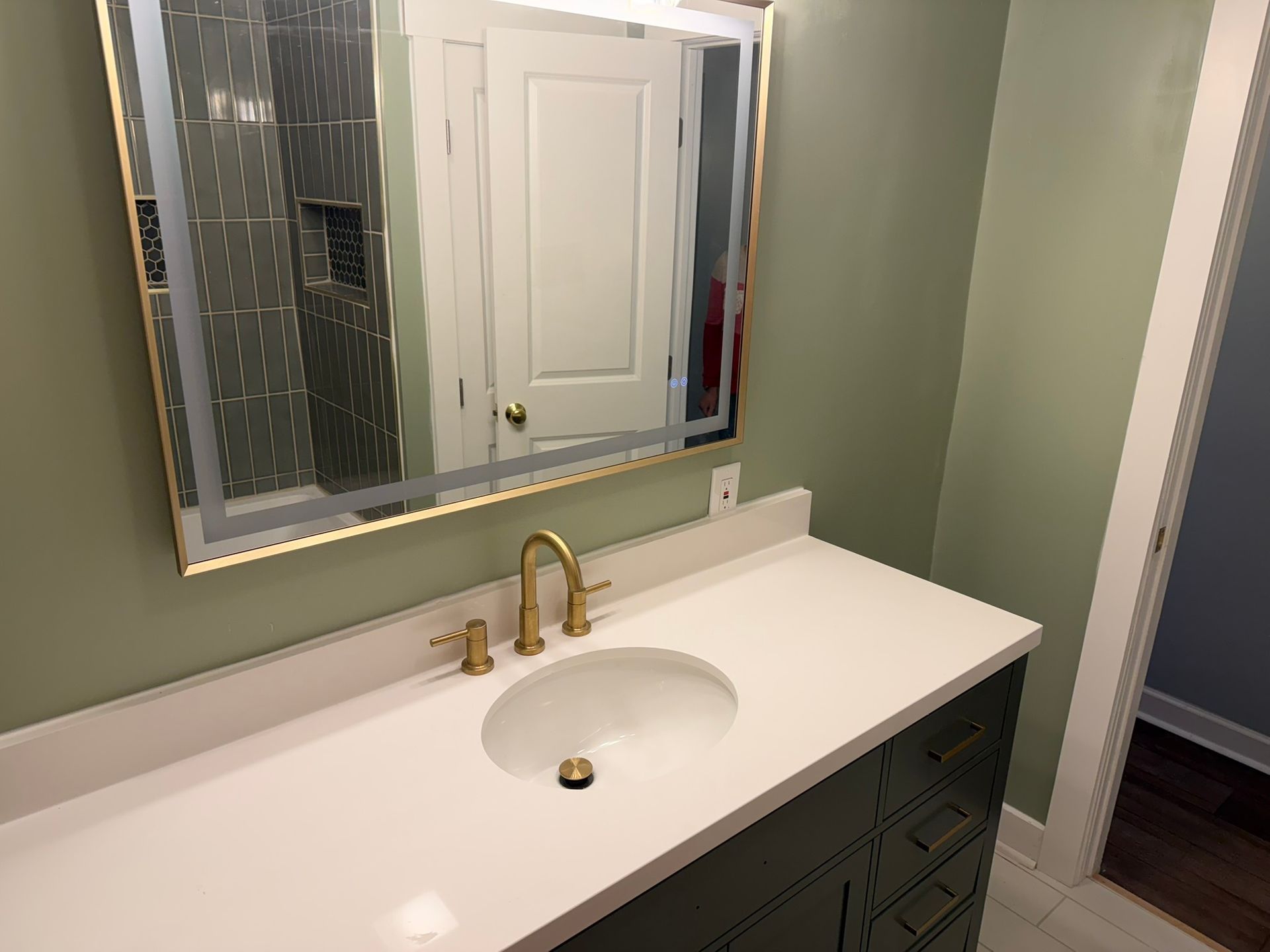 Bathroom vanity with white sink, brass faucet, mirror, and green walls