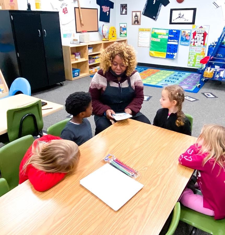 Teacher reads to four children seated at a table in a classroom.